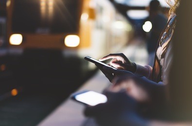 enjoying travel. young woman waiting on station platform on background light electric moving train using smart phone in night. tourist text message and plan route of stop railway, railroad transport