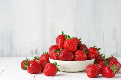 heap of fresh strawberries in ceramic bowl on rustic white wooden background. 