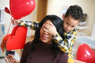 african american boy holding his mother closed eyes. looking at camera.