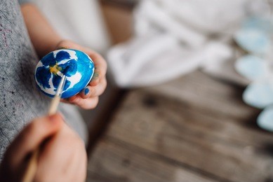 happy easter! cute little child girl painting with blue and yellow colors easter eggs. family preparing for easter. hands of a girl with a easter egg. close-up