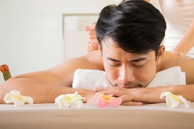 man is being pressing by herbal ball in spa.
