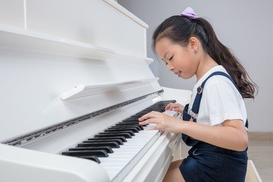 happy asian chinese little girl playing classical piano in the living room at home