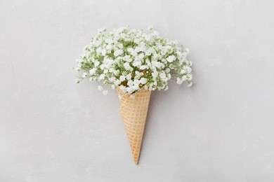ice cream of gypsophila flowers in waffle cone on light gray table top view in flat lay style