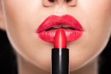 close-up partial view of young stylish woman applying red lipstick on black  