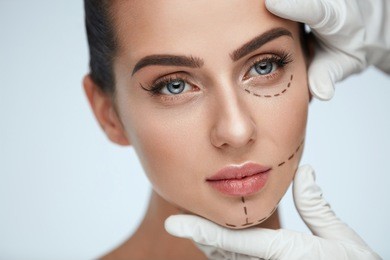 facial beauty treatment. beautiful young female with smooth skin, perfect makeup and surgical lines. closeup of beautician hands touching woman face before plastic surgery operation. high resolution