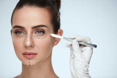 beauty operation. closeup of beautician hand with scalpel near young woman face. portrait of beautiful woman with perfect makeup and surgical lines on soft skin. facial treatment. high resolution