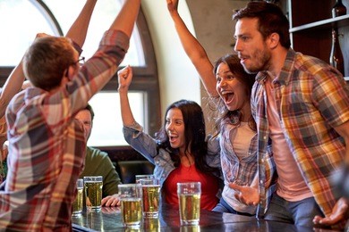 sport, people, leisure, friendship and entertainment concept - happy football fans or friends drinking beer and celebrating victory at bar or pub