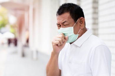 a asian old man wearing a face mask in the city coughing