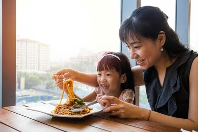 asian chinese mother and daughter eating spaghetti bolognese in the restaurant.