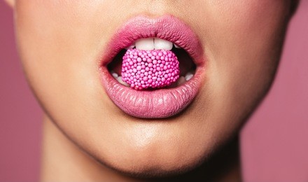 beautiful pink lips with a piece of sweet candy. close up of young woman with candy in mouth.