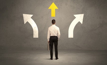 a confused businessman facing a grey urban wall with a yellow arrow pointing in the right direction concept