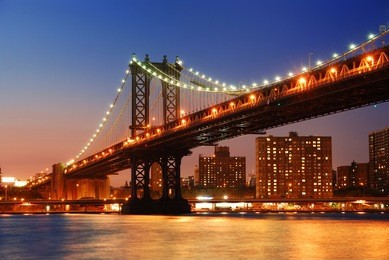 new york city manhattan bridge over hudson river with skyline after sunset night view illuminated with lights viewed from brooklyn.