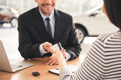 visiting car dealership. handsome sales manager is taking a credit card from the client and smiling