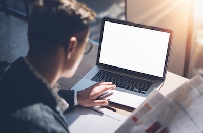 closeup view of banking finance analyst in eyeglasses working at sunny office on laptop while sitting at wooden table.businessman analyze stock report on notebook screen.blurred,horizontal mockup
