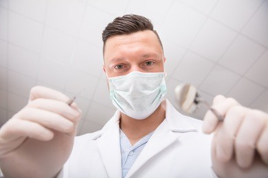first person view of a male dentist with dental mirror and hook in a clinic
