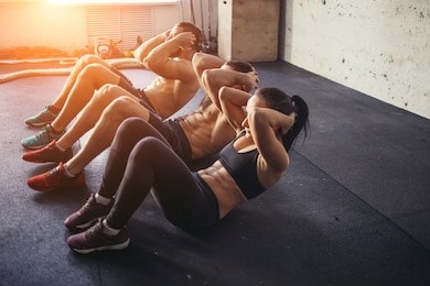 group of athletic adult men and women performing sit up exercises to strengthen their core abdominal muscles at fitness training