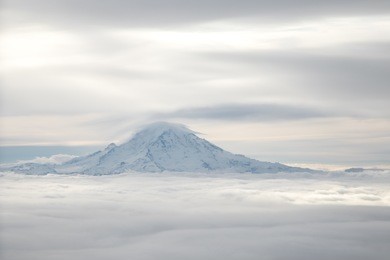 mt rainier snow covered peak summit on horizon between sea of fluffy white clouds blanketing the ground and sky in elevated drone aerial photography 