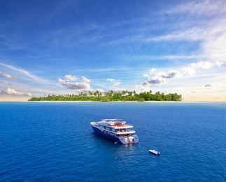 big safari luxury yacht sailing on ocean in maldives, tropical island on background. concept of travel vacation and vessel trip