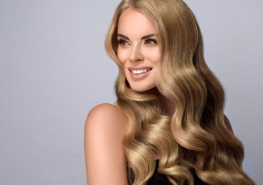 blonde  girl with long  and  volume shiny wavy hair .  beautiful  woman model with curly hairstyle .