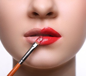 make-up artist apply lipstick with brush. close-up of female model face with fashion glossy red lips makeup, beauty concept