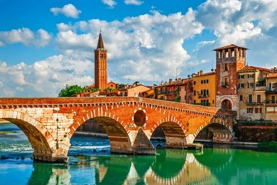 panoramic view to bridge ponte pietra in verona on adige river, veneto region, italy. sunny summer day panorama and blue dramatic sky with clouds. ancient european italian terracotta color houses.