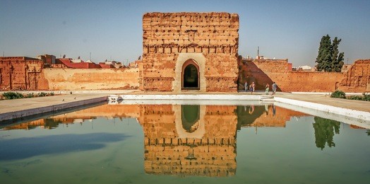 badi palace in marrakech with reflection in water pond in front and tourists in the background