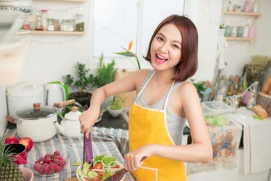 young asian woman making salad in kitchen smiling and laughing happy at home.