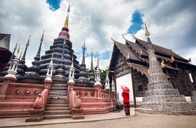 woman with red traditional thai umbrella looking at black temple wat phan tao made from wood in chiang mai, thailand