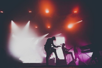 music band / group with guitar player / guitarist silhouette perform on a concert stage.  dark background, smoke, concert  spotlights
