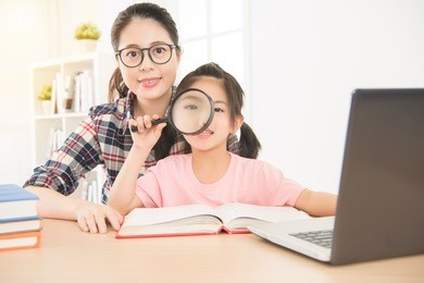 portrait of glasses woman teacher and young girl children studying with magnifier and pc reading. little daughter use glass let eye become bigger.