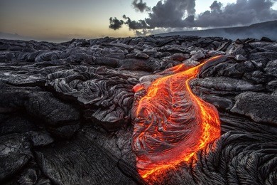 red orange vibrant molten lava flowing onto grey lavafield and glossy rocky land near hawaiian volcano with vog on background