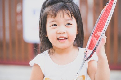 little asian girl playing badminton with her father in front of the house.