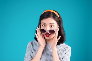 smiling asian woman dressed in pin-up style dress wearing eyeglasses over blue.