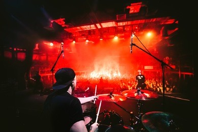 band on stage. drummer playing drum set at concert on stage. music show. bright scene lighting in club,drum sticks in hands.fans burn red flares at rock concert. view from the stage to the drummer. 