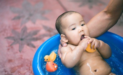father take a shower his baby in blue bath and toys float on the water