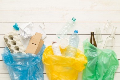 recycling and ecology. sorting (segregating) household waste (paper, glass, plastic) into bags captured from above (flat lay). white wooden background with free text (copy) space.