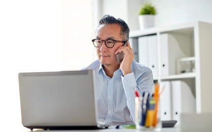 business, people, communication and technology concept - businessman with laptop computer calling on smartphone at office