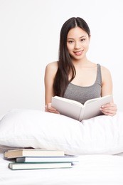 a shot of a beautiful asian college student reading on her bed