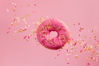 sprinkled pink donut. frosted sprinkled donut on pink background.