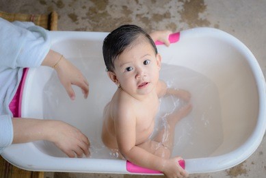 happy baby taking a bath playing with mother washing little boy. young child in a bathtub.