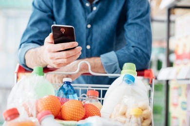 man shopping at the supermarket, he is leaning in the shopping cart and connecting with his mobile phone