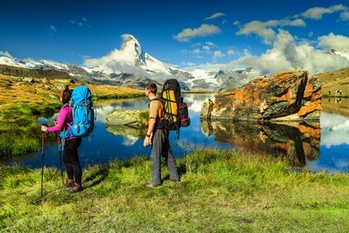 young couple walking with backpack and camping equipment on the mountain trail, near stellisee lake, valais region, zermatt, switzerland, europe