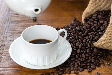coffee beans inside gunny sacks spilled on wooden table with white cup and pot