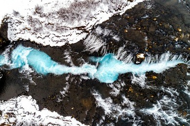 aerial view of beautiful bruarfoss waterfall with turquoise water and snow in winter, south iceland