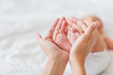 mother holds newborn baby's bare feet. tiny feet in woman's hand. cozy morning at home.
