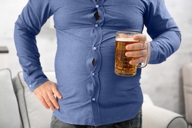 man with big belly holding glass of beer at home