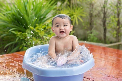 cute baby boy taking bath outdoors and playing in a bath with toys.