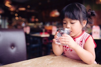 happy adorable little girl drinking water.smiling asian kid holding transparent glass in her hand.