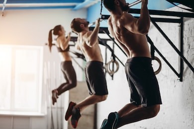 group of six attractive young male and female adults doing pull ups on bar in cross fit training gym with brick walls and black mats