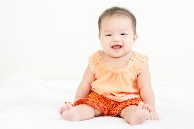 portrait of a little adorable infant baby girl sitting on the bed and smiling to camera with copyspace